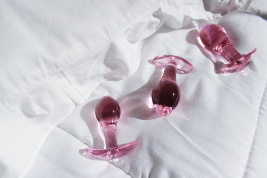 Set of three pink glass t bar butt plugs laid out on a white blanket.