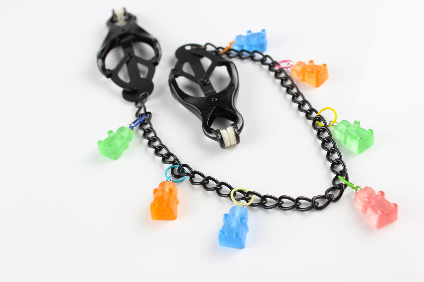 Black Japanese clover clamps with a black chain connecting the clamps and 6 colorful gummy bear charms hanging off the chain placed on a white background.