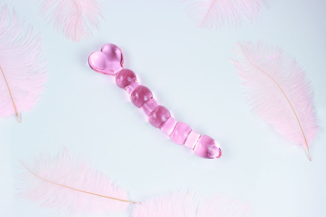 Pink glass anal bead dildo with heart shaped base on white background with pink feathers