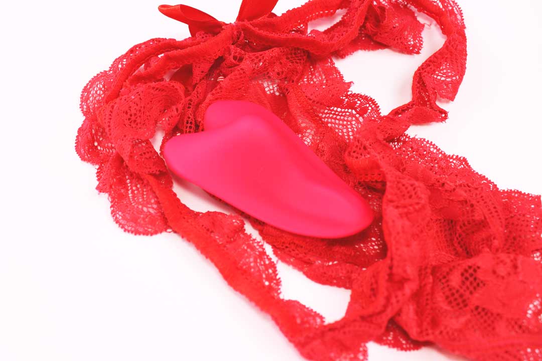 red heart shaped silicone remote controlled panty vibrator laying face down in red lingerie on a white background.