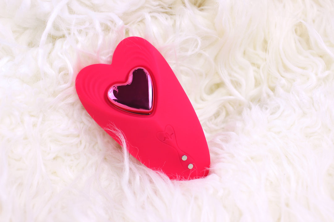 Red heart shaped silicone panty vibrator and remote laying in a fluffy white blanket.