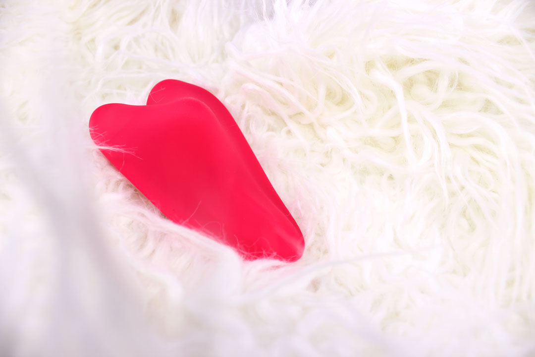 red heart shaped panty vibrator laying face down in a white fluffy blanket.