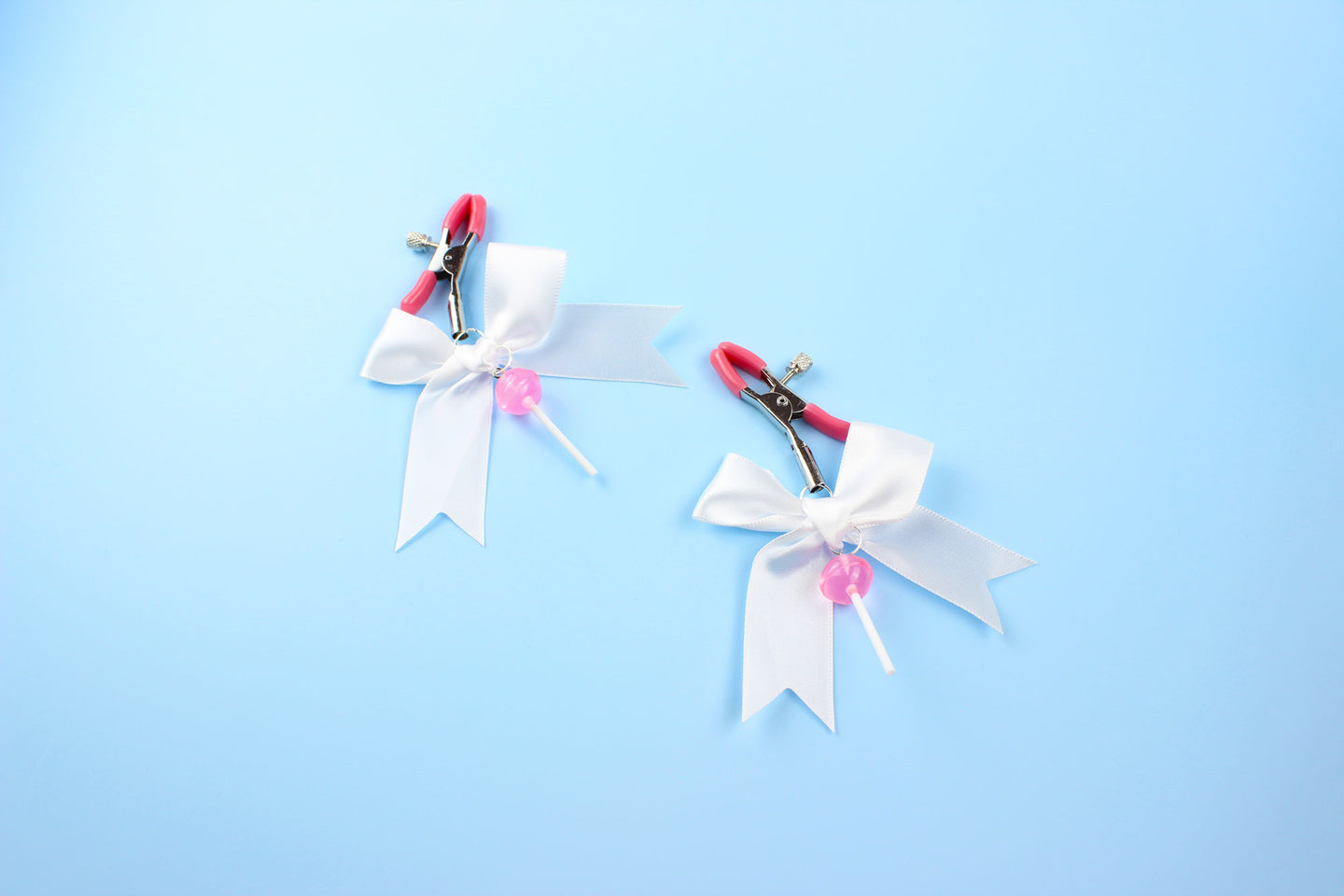 Pink grip silver screw nipple clamps with a white bow and a pink lollipop hanging off of each clamp in front of a blue background.