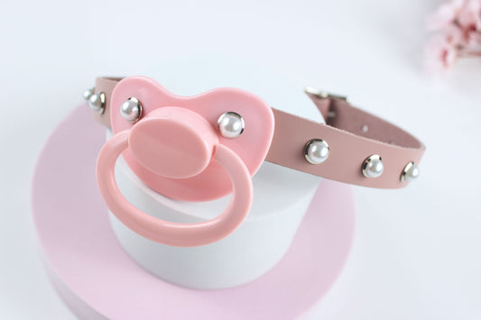 Pink pacifier gag with pearl rivets on a white and pink circular stand