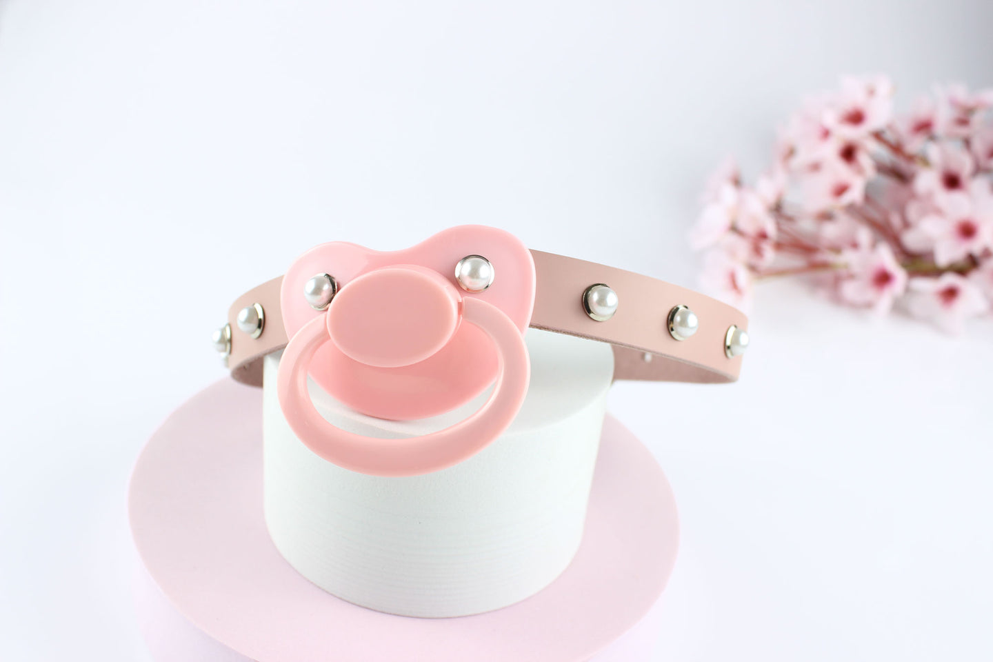 Pink pacifier gag with pearl rivets on a white and pink circular stand