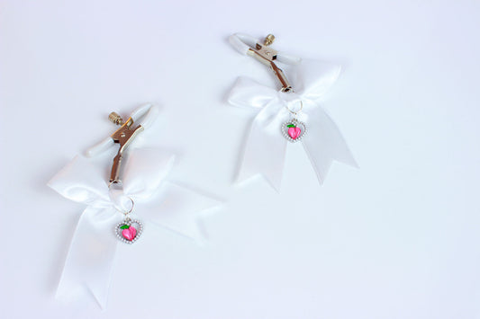 Two screw clamps with white PVC grip caps, white bows, and pearl heart bordered peach charms laid on white background