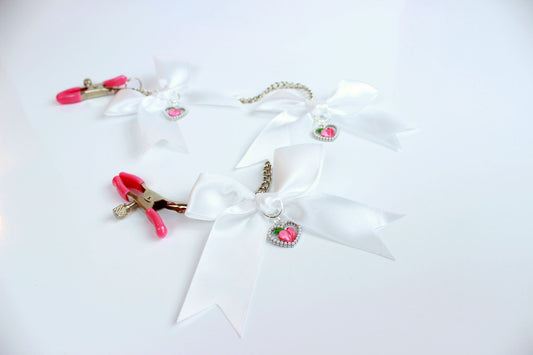 Front view of adjustable screw clamps with pink grip caps connected by chain with white bows and heart shaped peach charms