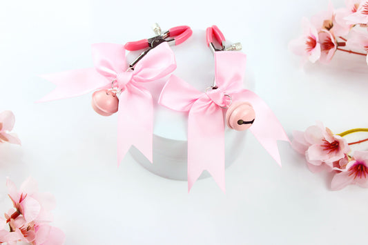 Two adjustable nipple clamps with pink caps, bows, and bells on a white background