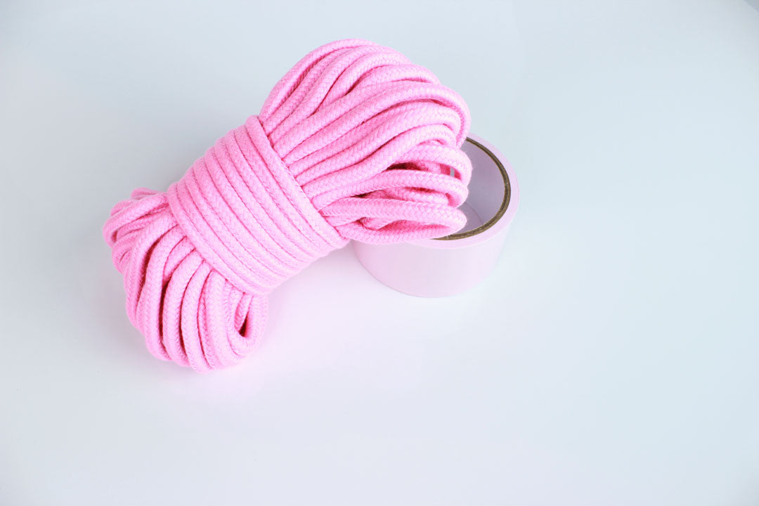 65 foot pink cotton shibari rope and roll of light pink bondage tape on white background