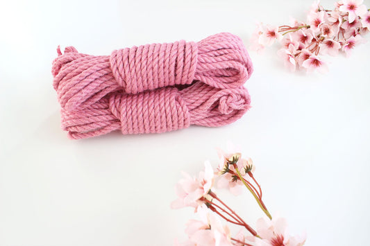 Two bundles of pink jute rope on a white background with pink flowers around the border.