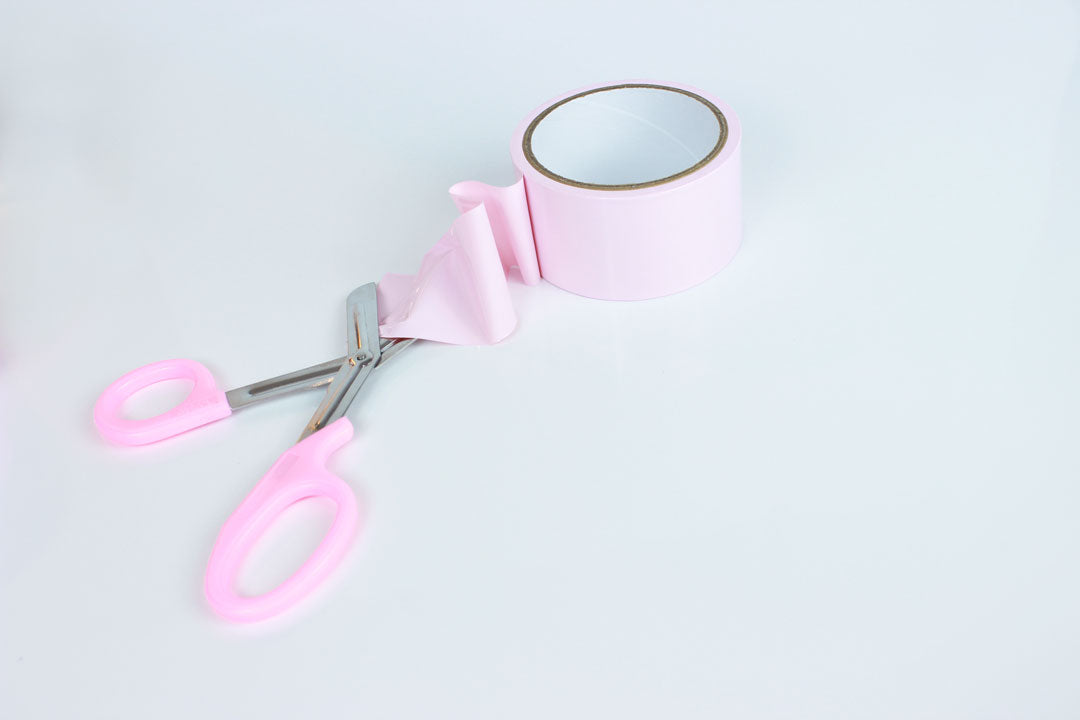 trauma shears with pink handles cutting pink bondage tape