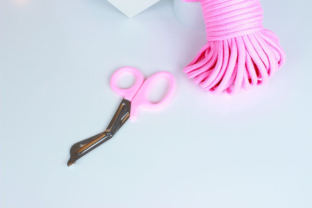 Bondage shears with light pink handles and pink rope in corner on white background