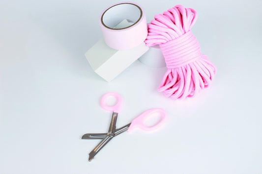 Pastel pink bondage tape, 65 foot cotton rope, and bondage shears on white background