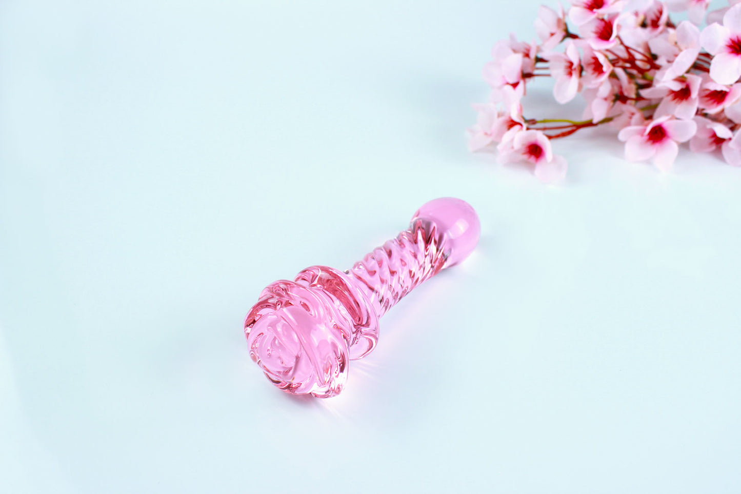 Pink glass dildo with a rose base and a ridged shaft on white background.