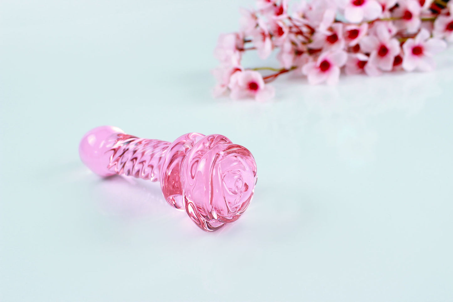 Pink glass dildo with a rose base and a ridged shaft on white background.