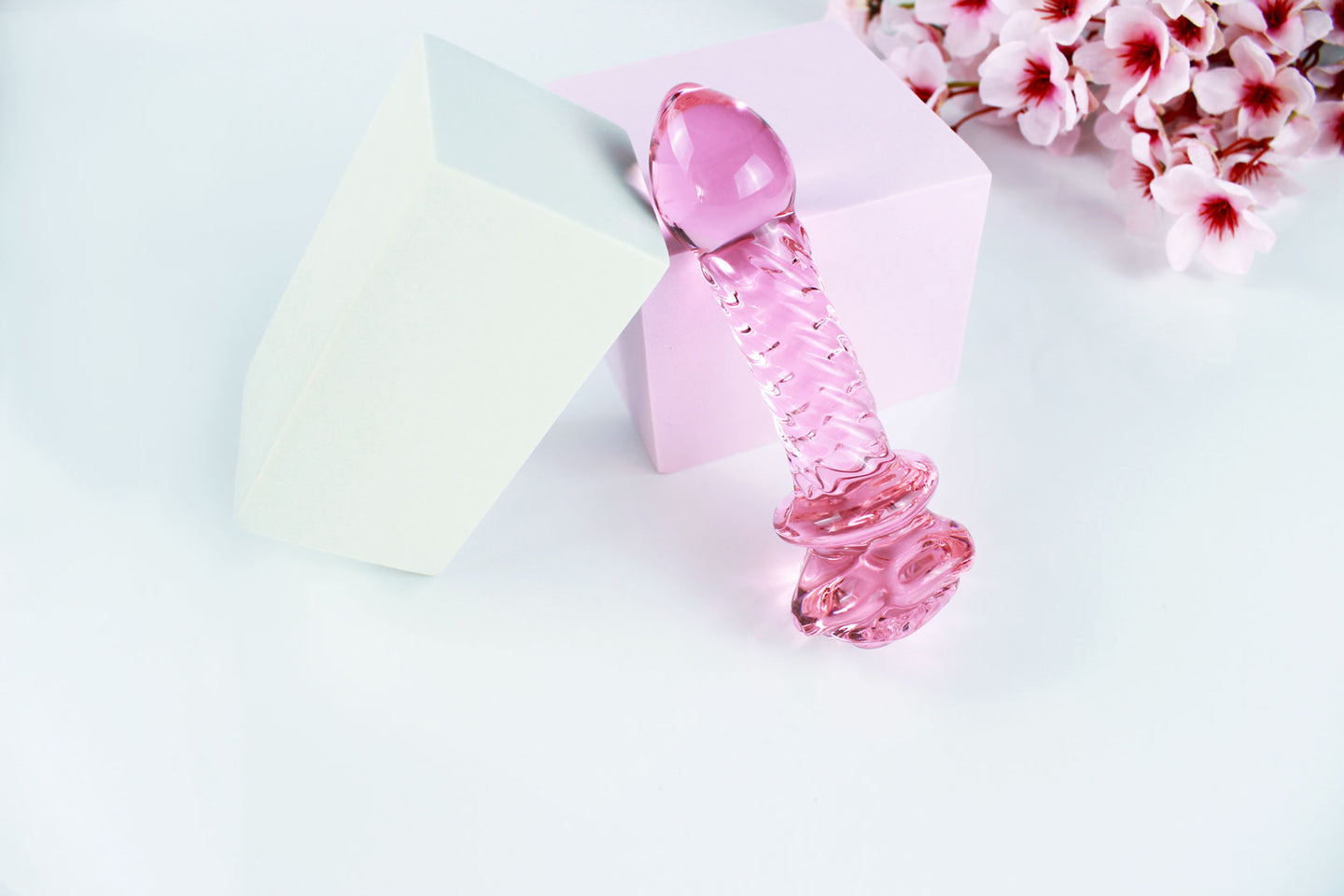 Ridged glass rose dildo standing on its base over white background