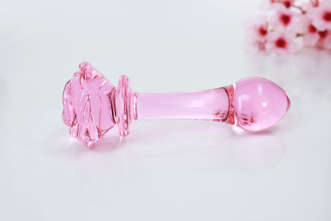 Pink glass butt plug with a rose base against a white backdrop with flowers.