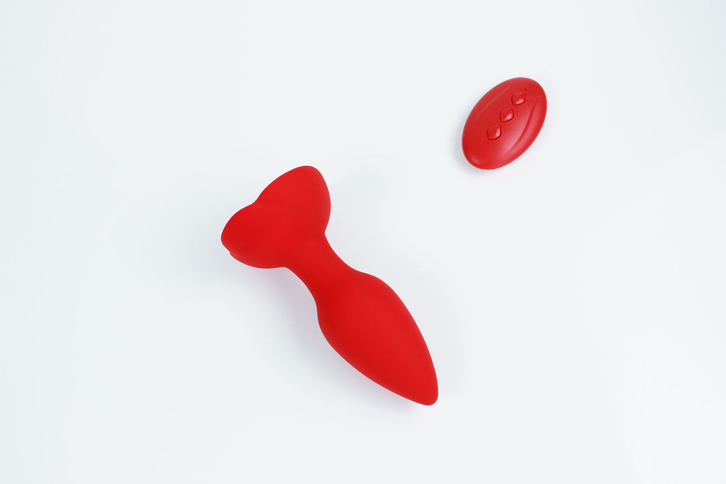 Down shot of red vibrating butt plug with rose base and remote control on a white background 