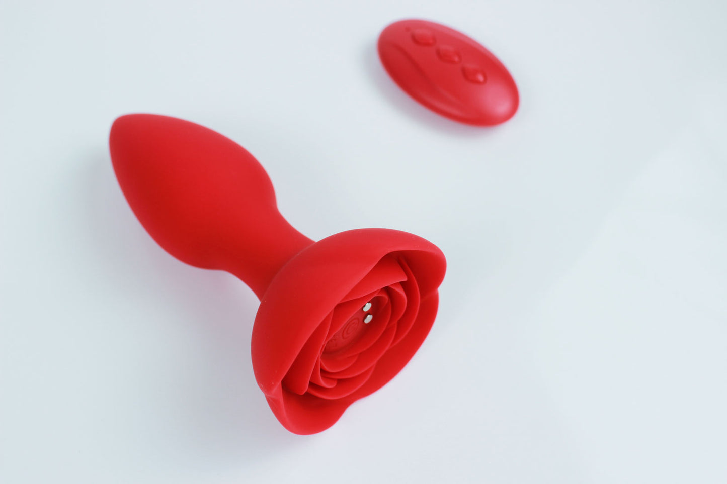 Red vibrating butt plug with rose base and remote control on a white background 