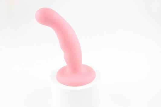 Light pink silicone dildo standing upright on white background