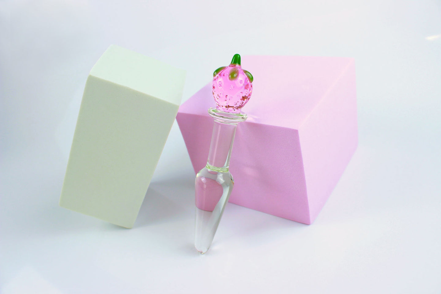Strawberry tapered glass butt plug against a pink block and white background.