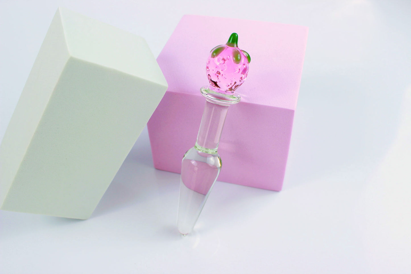 Strawberry tapered glass butt plug against a pink block and white background.