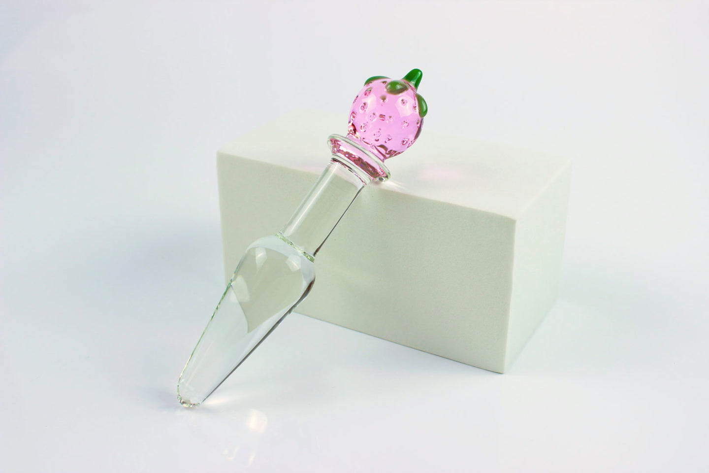 Strawberry tapered glass butt plug on a white stand and white background.