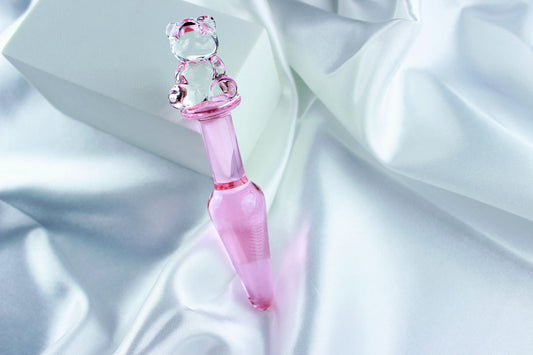Bear glass butt plug with a pink tapered shaft and clear bear base on a white satin background