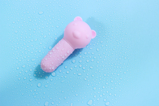 Pink bear bullet vibrator with water droplets on blue background.