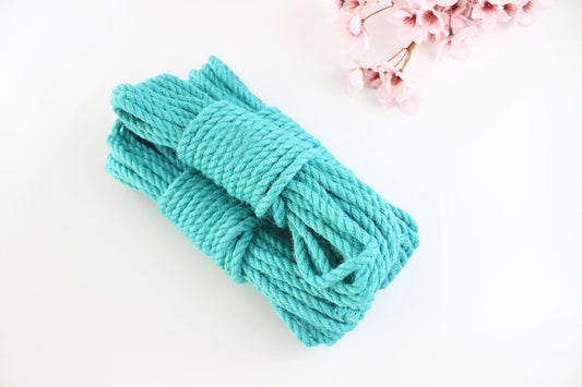 Multiple bundles of turquoise jute rope stacked on top of each other against a white background with pink flowers.