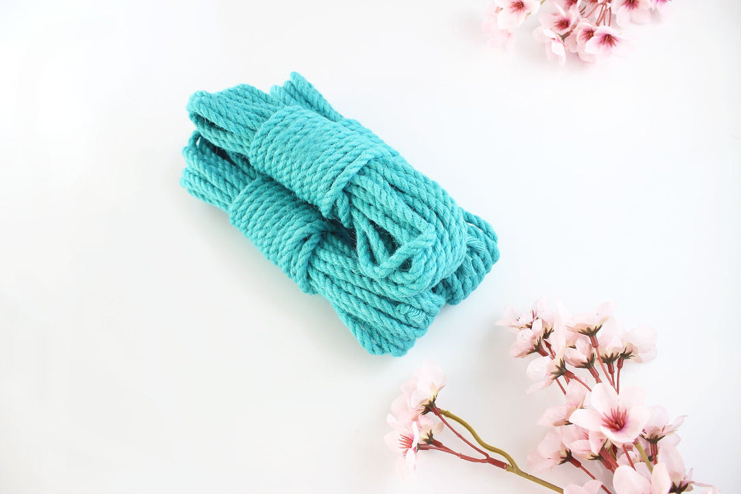 Multiple bundles of turquoise jute rope stacked on top of each other against a white background with pink flowers.