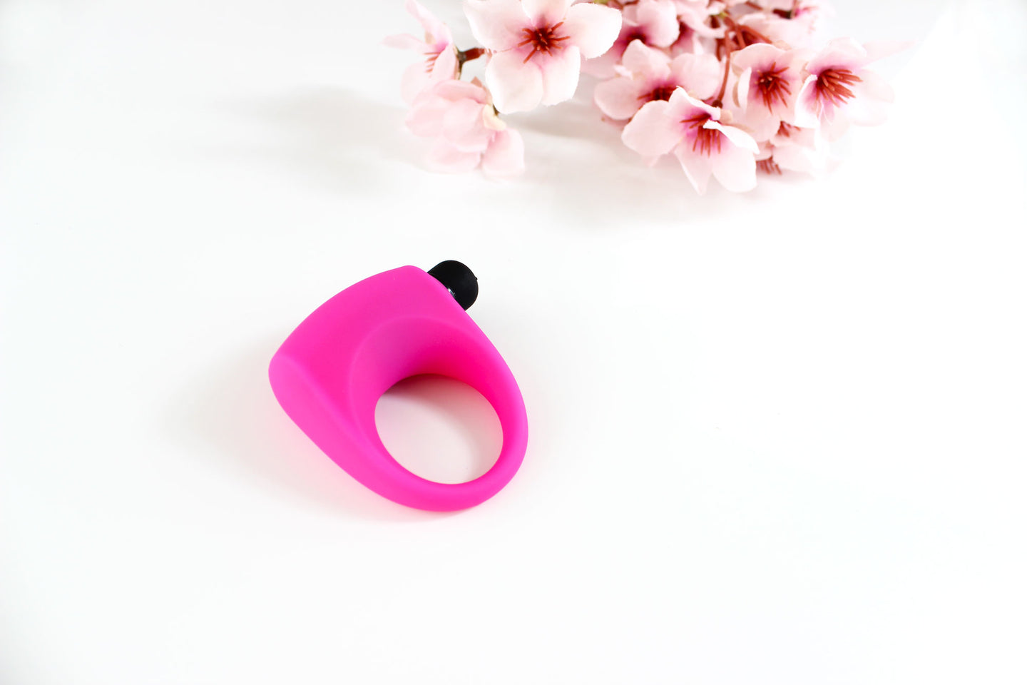 Hot pink silicone vibrating cock ring on white background with pink flowers in the corner