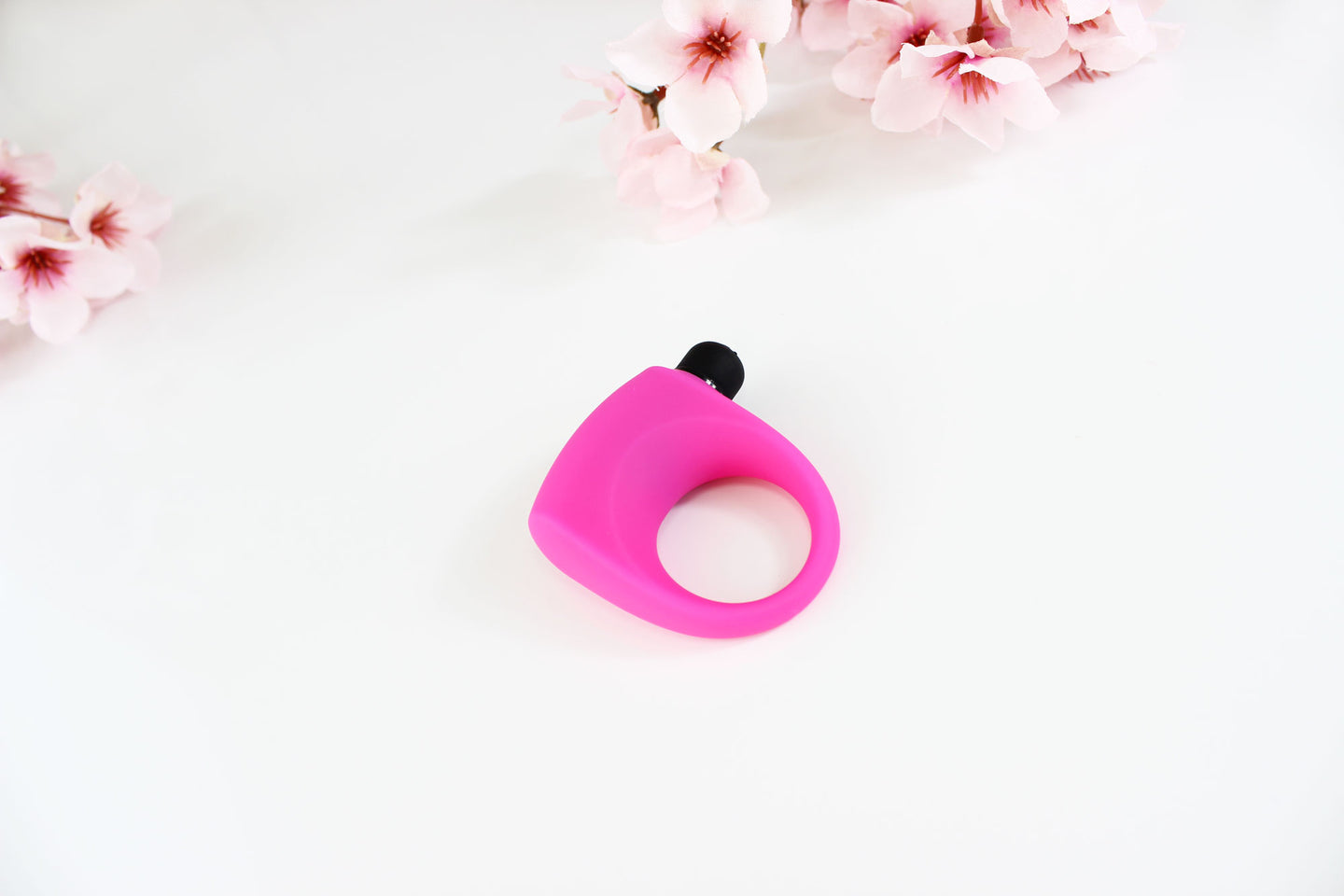 Hot pink silicone vibrating cock ring on white background with pink flowers in the corner