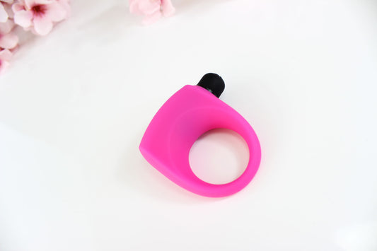 Hot pink silicone vibrating cock ring on white background with pink flowers in the corner