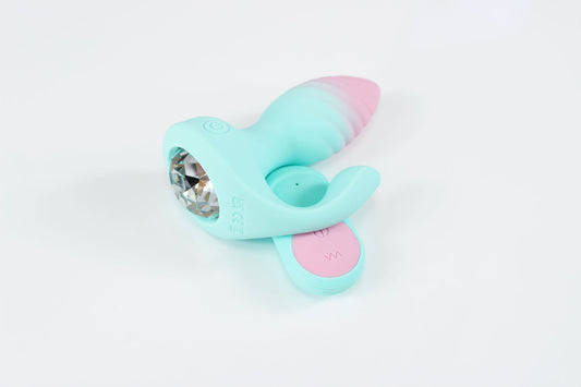 Side view of pastel blue and pink vibrating gem butt plug with remote on white background
