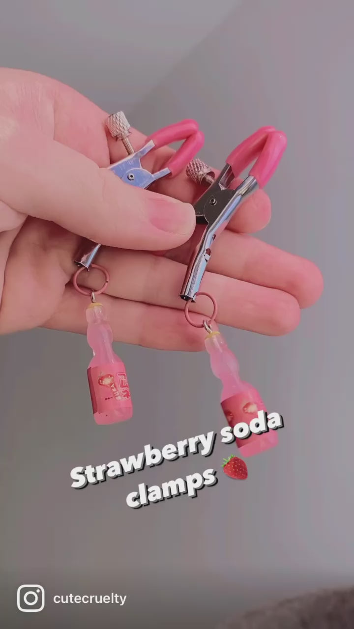 Video of hands dangling a pair of pink and silver adjustable screw nipple clamps with Japanese strawberry Ramune soda charms