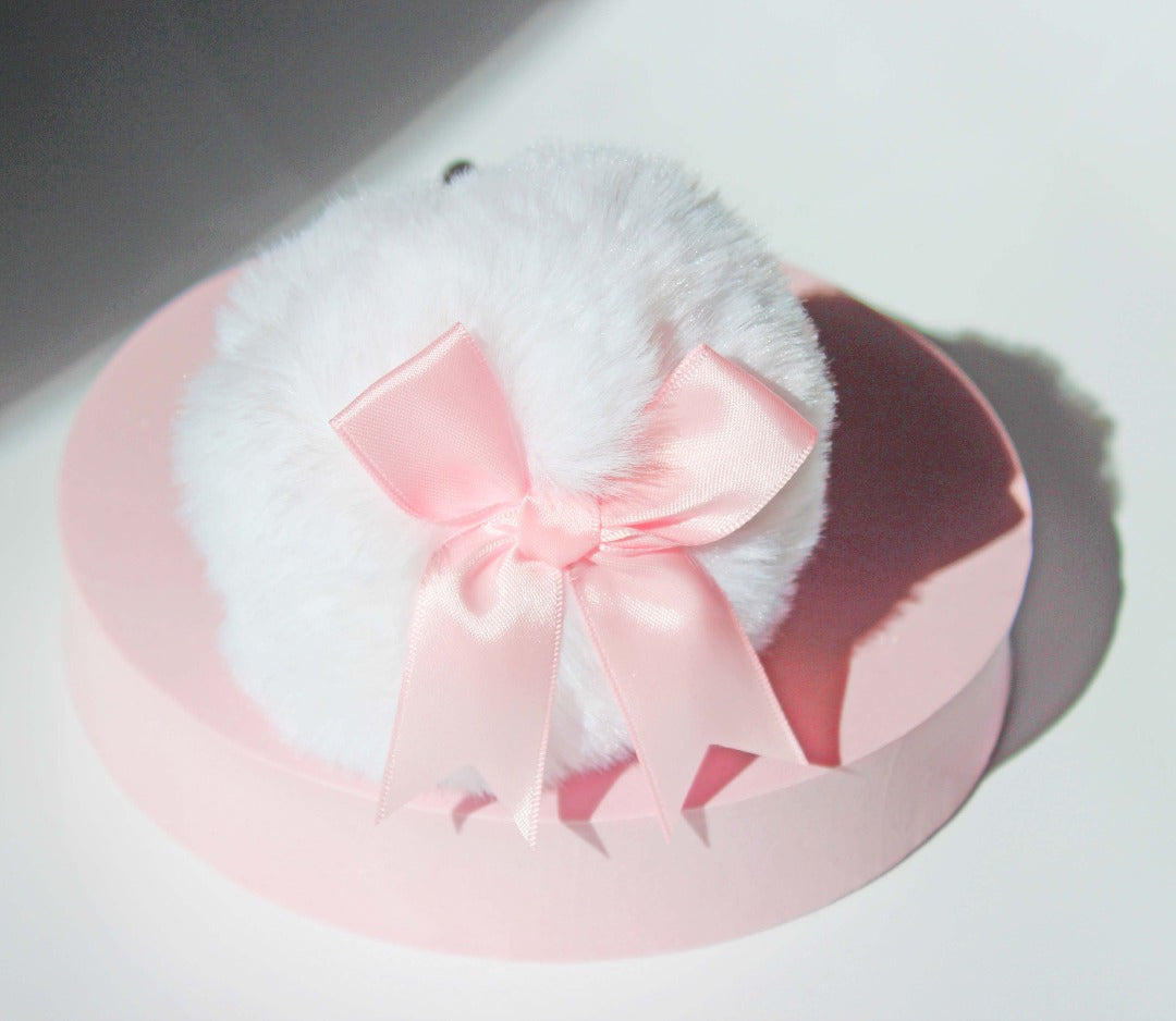 cute white bunny tail glass butt plug with a pink bow on the pom on a pink stand against a white background.