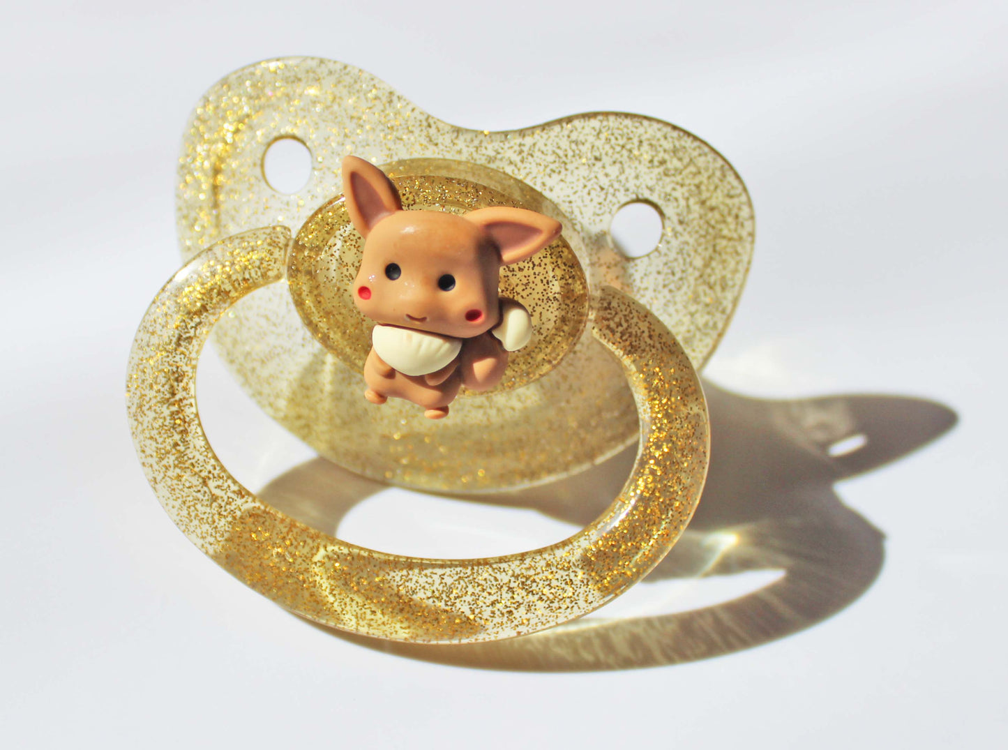 Gold adult pacifier with a fox charm on a white background.