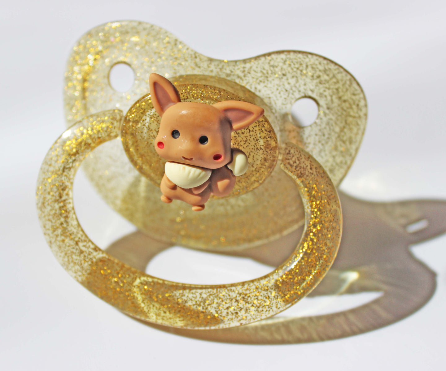 Gold adult pacifier with a fox charm on a white background.