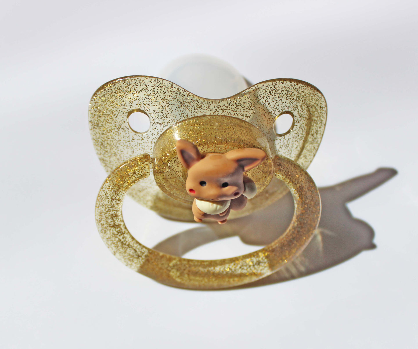 Gold adult pacifier with a fox charm on a white background.