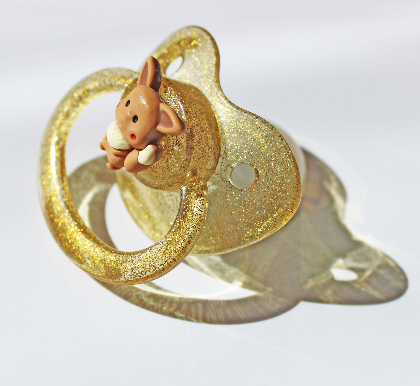 Gold adult pacifier with a fox charm on a white background.