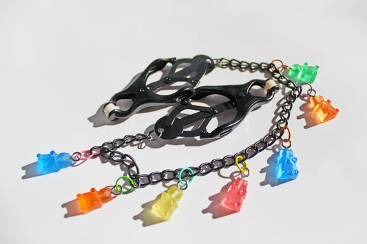 Black Japanese clover clamps with a black chain connecting the clamps and 6 colorful gummy bear charms hanging off the chain placed on a white background.