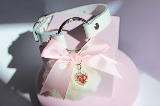 Kawaii white pom collar with a pink bow, heart, and white pom on a pink stand with a white background.