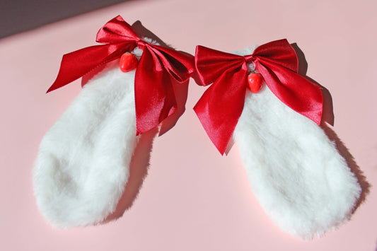 Set of white lop bunny ears with red bows and strawberries at the top of them on a pink background.