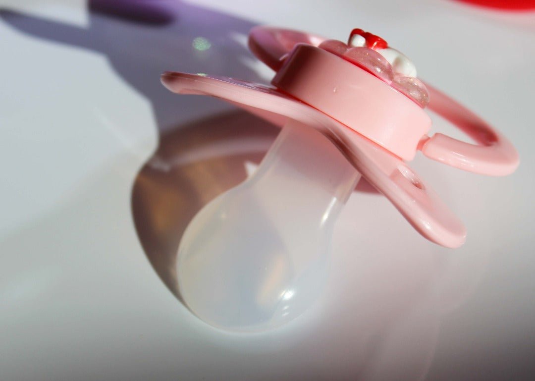 Pink adult pacifier with flower kitty deco charm turned around to show the binkie on a white background.