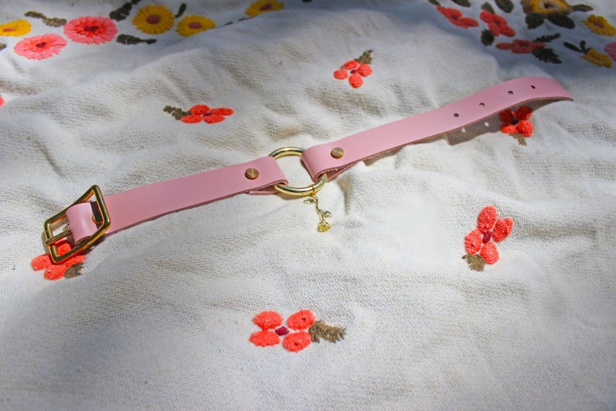 Pink leather rose submissive collar with gold hardware laid out to show the length of the collar set on a blanket.