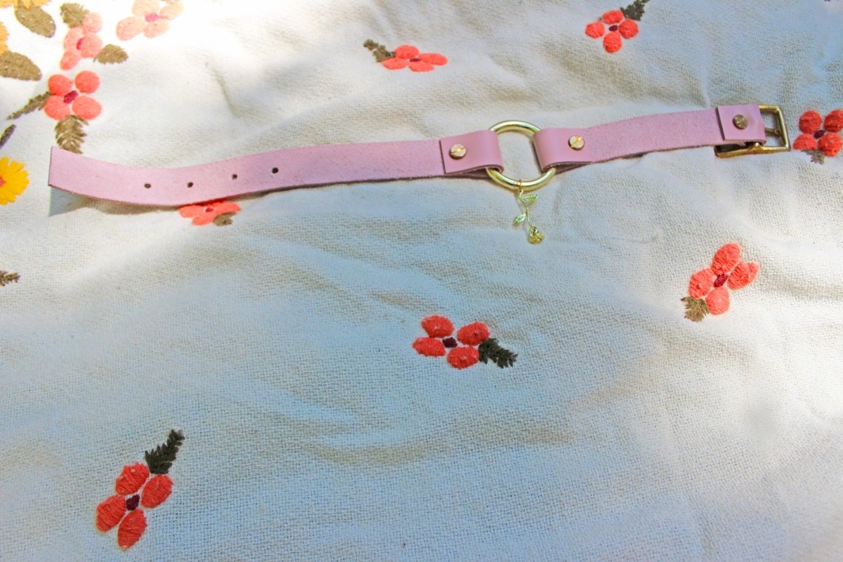 Pink leather rose submissive collar with gold hardware laid out to show the length of the collar set on a blanket.