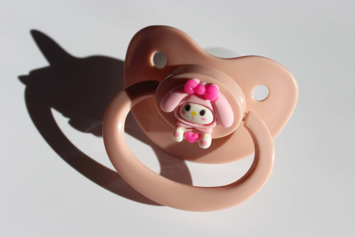 kawaii pink adult pacifier with bunny charm on a white background.