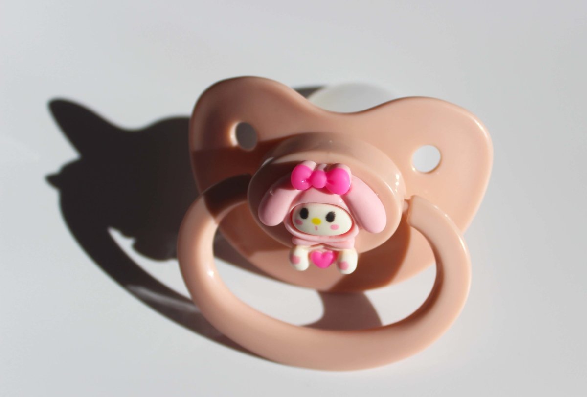 kawaii pink adult pacifier with bunny charm on a white background.