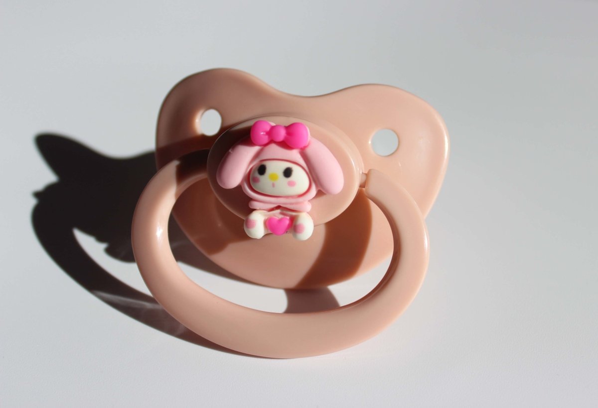 kawaii pink adult pacifier with bunny charm on a white background.